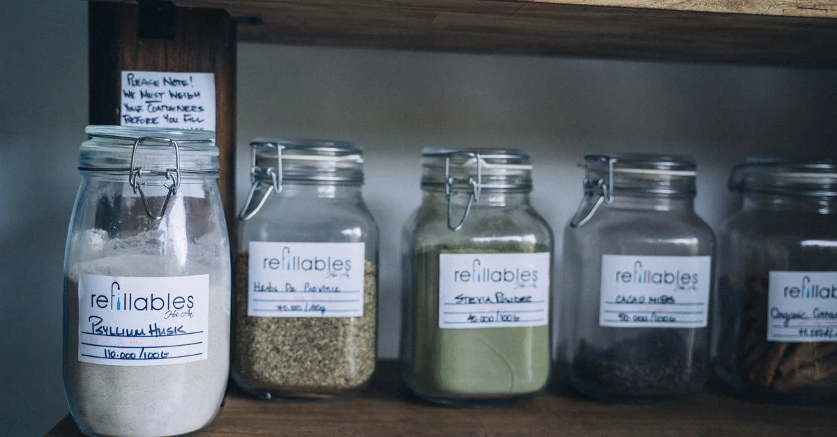 Bocaux en verre réutilisables avec des produits bio sur une étagère en bois.
