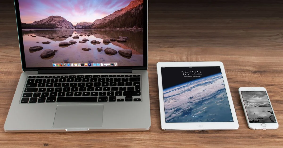 Espace de travail moderne présentant un ordinateur portable Apple, une tablette et un smartphone sur un bureau en bois.