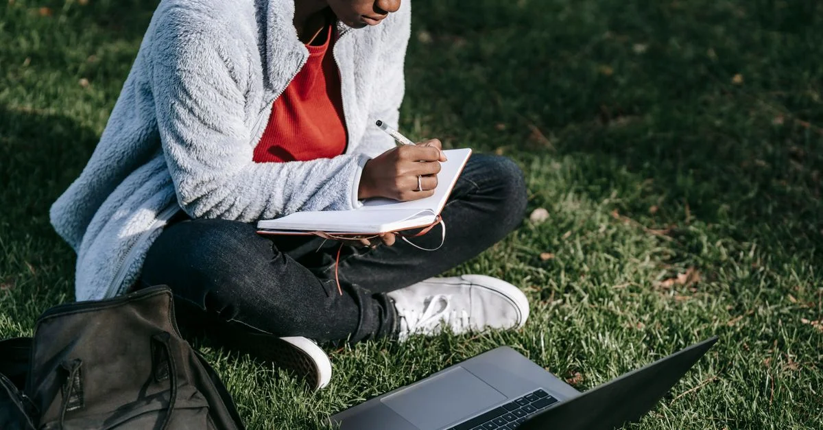 Une jeune femme qui se concentre sur ses devoirs en plein air dans un parc avec un ordinateur portable et un carnet.