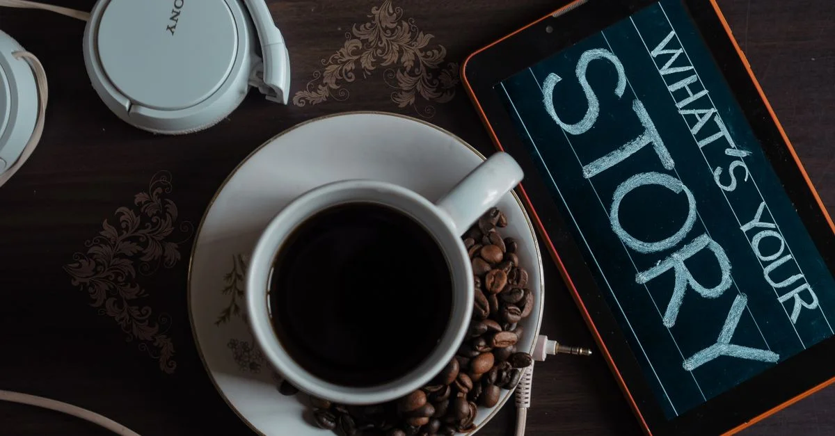 Plan de travail d'une tasse de café, écouteurs et tablette avec 'Quelle est votre histoire' à l'écran.