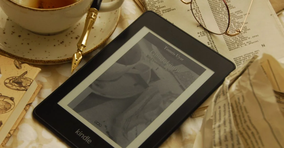 Un e-reader Kindle avec du thé et des lunettes vintage, créant une atmosphère de lecture confortable.