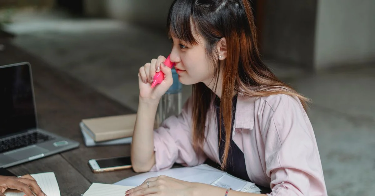 Femme asiatique concentrée sur ses études avec un ordinateur portable et un bloc-notes en plein air.