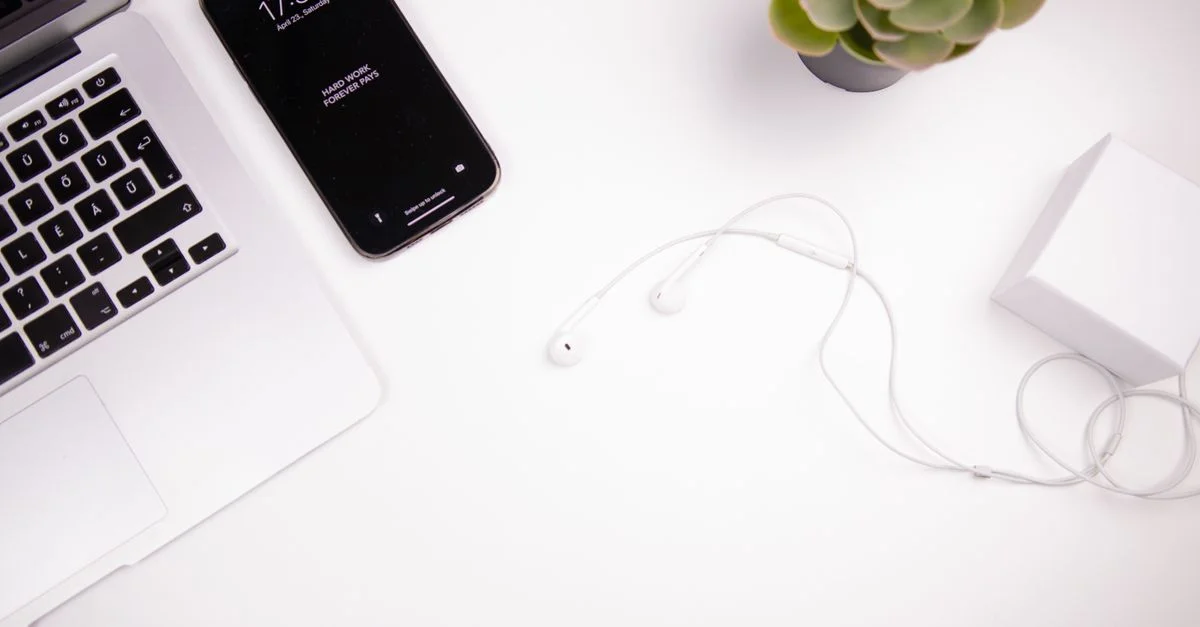 Espace de travail minimaliste élégant avec un ordinateur portable, un smartphone, des écouteurs et une plante succulente sur un bureau blanc.