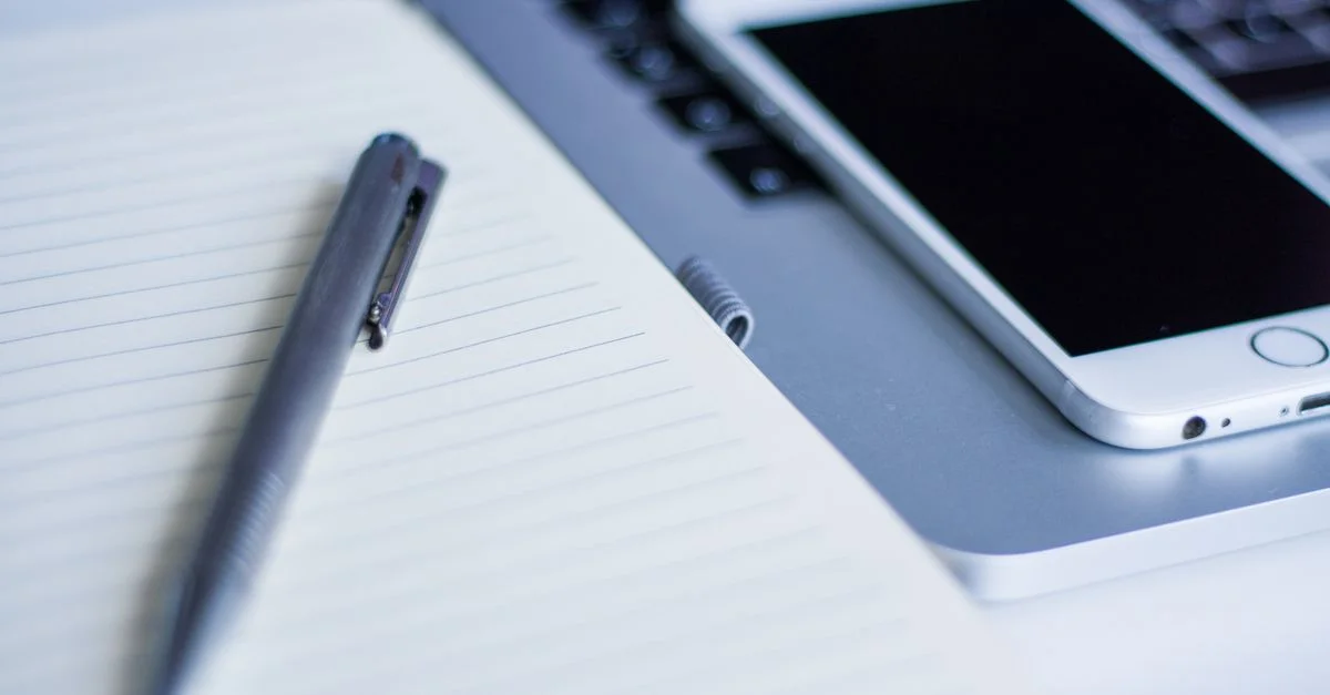 Gros plan sur un ordinateur portable, un smartphone et un stylo sur un bureau. Idéal pour des thèmes technologiques, de travail et de productivité.
