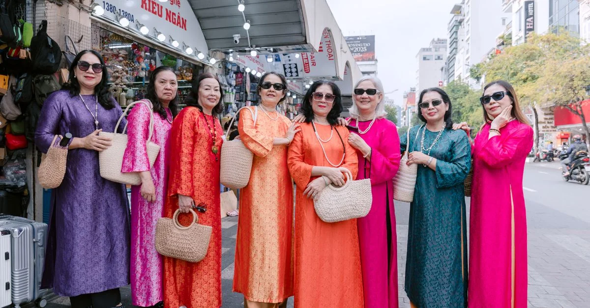 Des femmes vêtues de tenues traditionnelles Ao Dai colorées posent en souriant dans un paysage urbain.