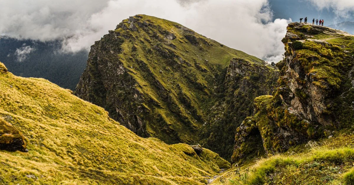 Des randonneurs se tenant sur un sommet de montagne verte sous un ciel nuageux, explorant la nature.