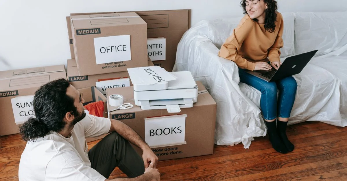 Jeune couple organisant des boîtes et se relaxant avec un ordinateur portable pendant le jour du déménagement à l'intérieur.