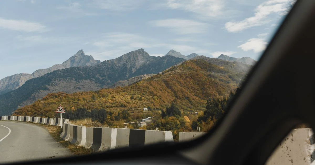 Vue d'une route de montagne avec un feuillage d'automne coloré à travers la fenêtre d'une voiture, capturant une expérience de voyage pittoresque.