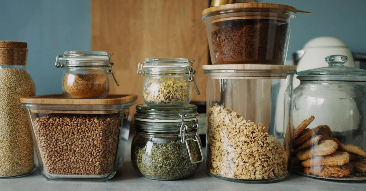 Aménagement de garde-manger élégant avec une variété d'aliments dans des bocaux en verre, mettant en avant des produits secs et des biscuits.